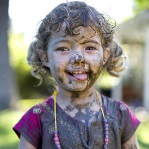 Girl (3-5) covered in mud, smiling