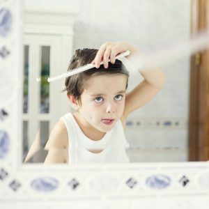 Boy (4-5) combing hair before mirror