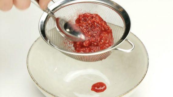 πιέζει τα σμέουρα με ένα κουτάλι αφού τα τοποθέτησε σε ένα σουρωτήρι με σκοπό να τα καλλιεργήσει μόνος του